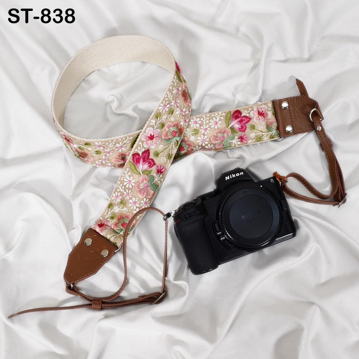 A floral-patterned camera strap and a black Nikon camera are placed on a white fabric surface.