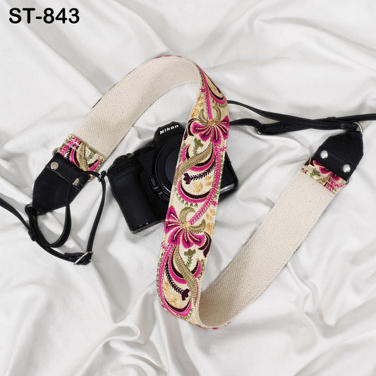 A black camera with a colorful floral patterned strap is placed on a white surface.