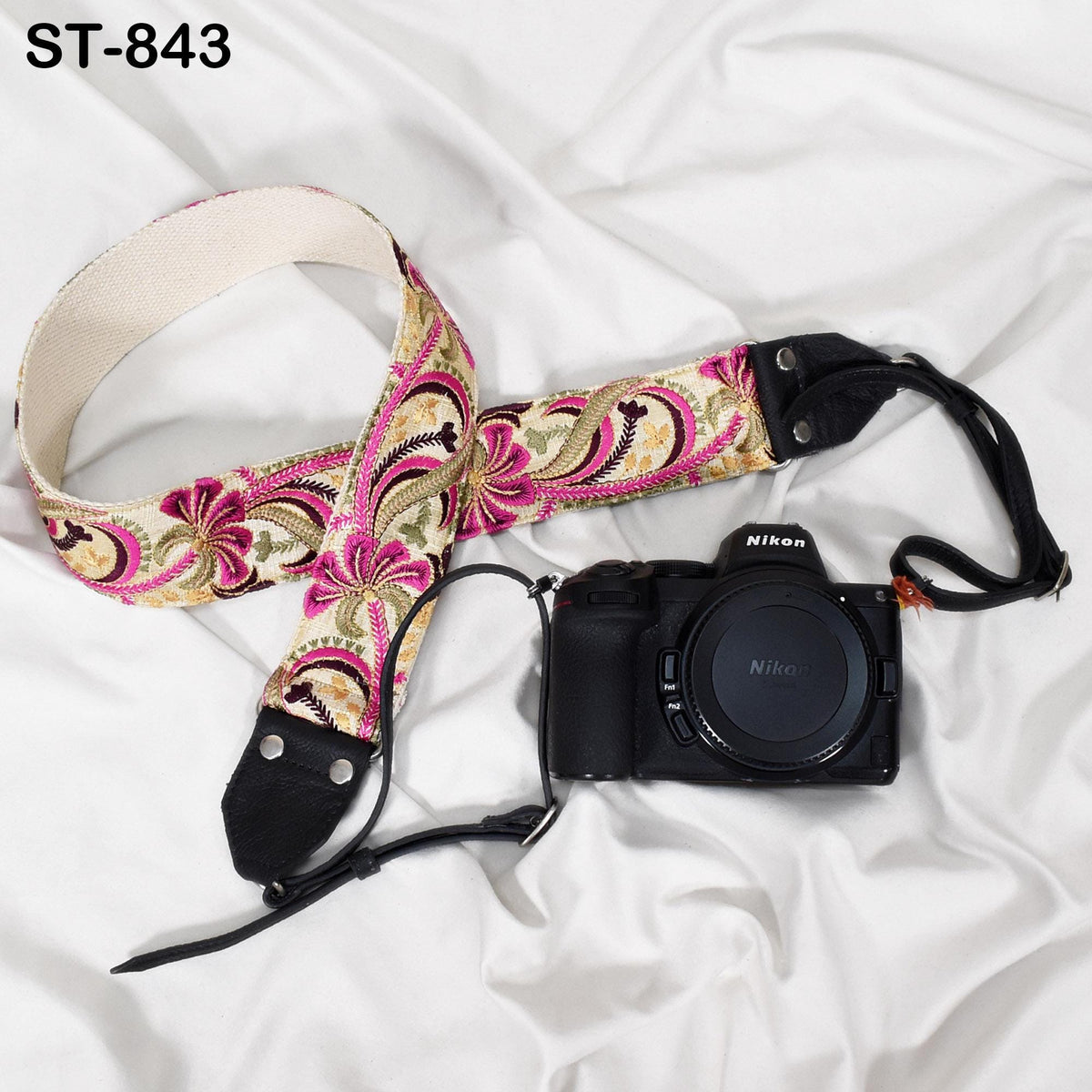 A floral patterned camera strap and a Nikon camera are placed on a white surface.