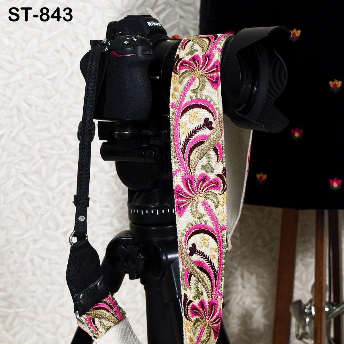 A black camera with a floral patterned strap is mounted on a tripod, with a blurred background.