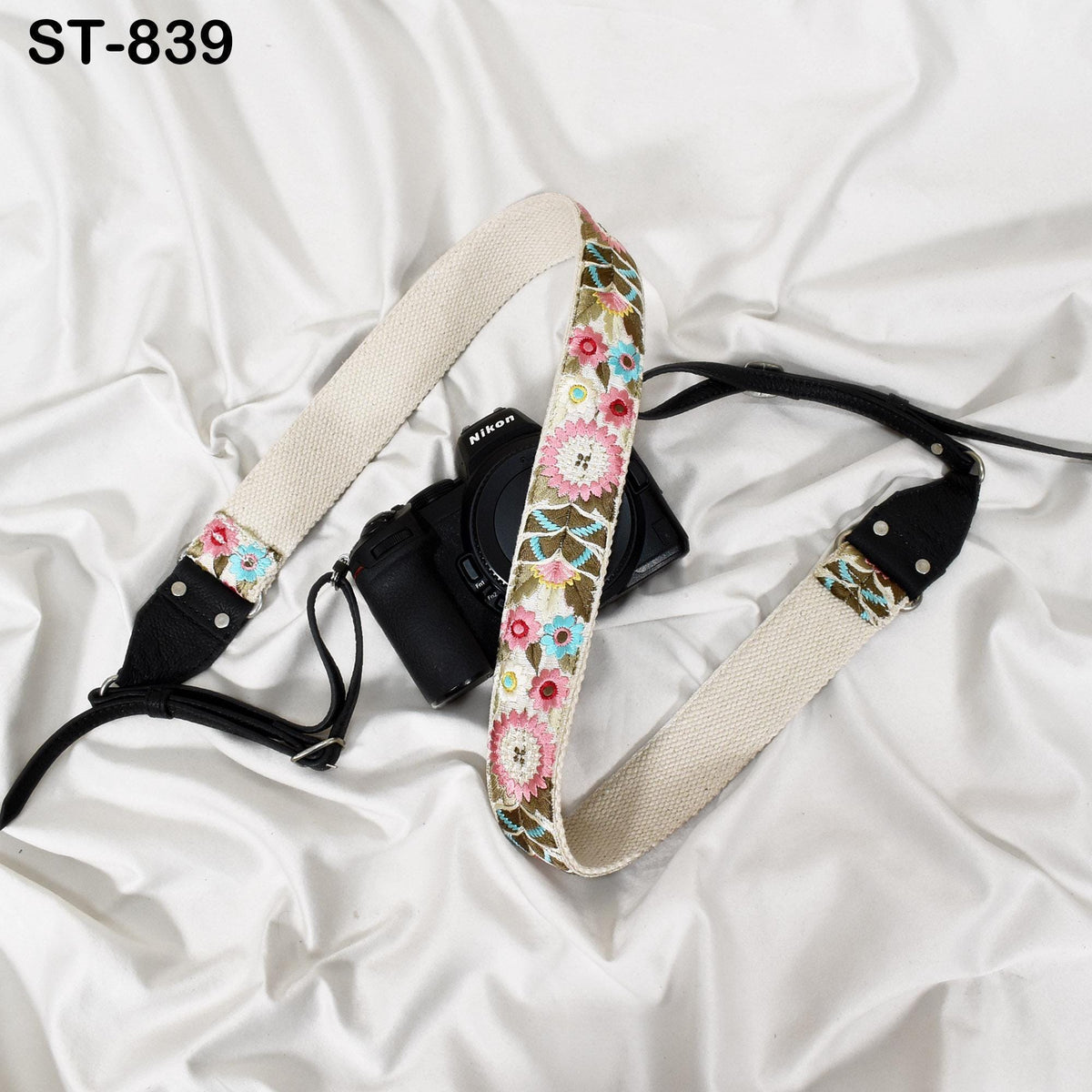 A black camera with a floral patterned strap is placed on a white surface.