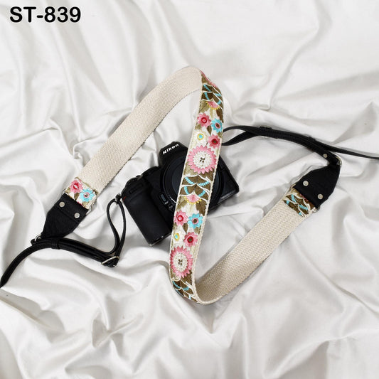 A black camera with a floral patterned strap is placed on a white surface.