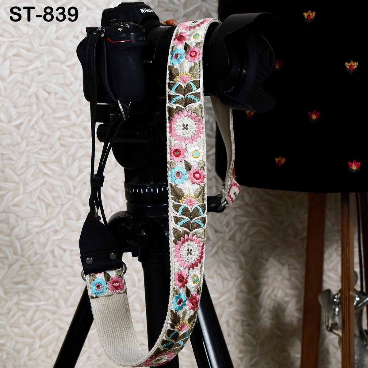 A black camera with a floral patterned strap attached to it, placed on a tripod.