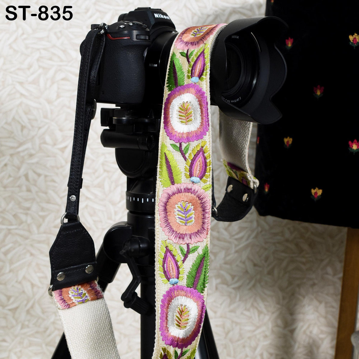 A black camera with a colorful floral patterned strap attached to it, placed on a tripod.