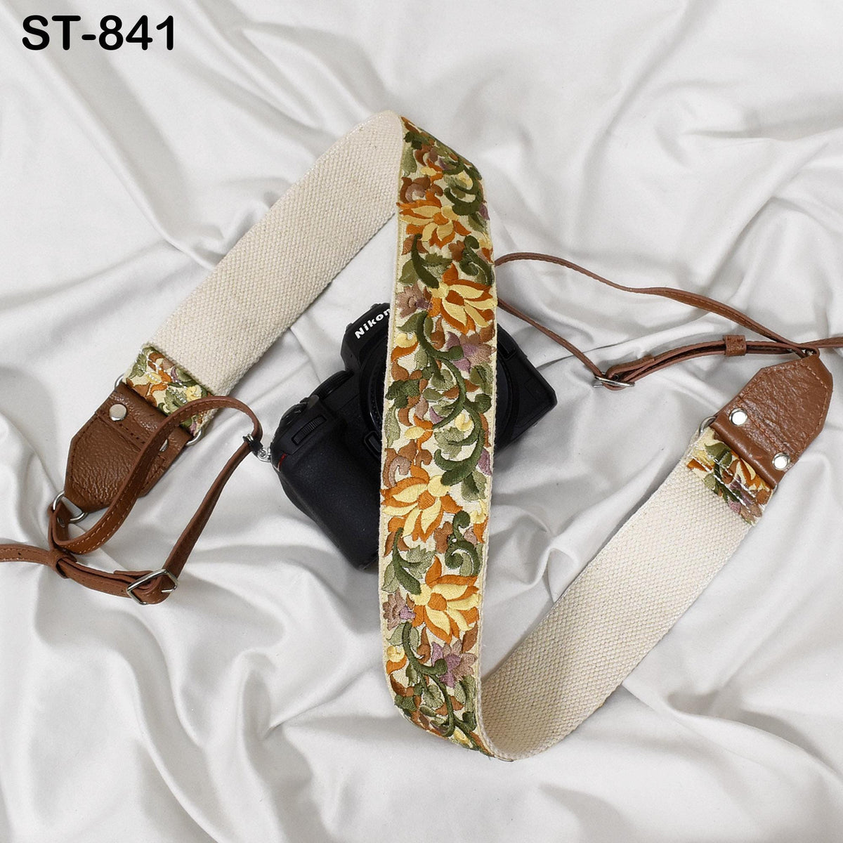 A floral patterned camera strap is draped over a black camera, with a brown leather strap attached to the camera.