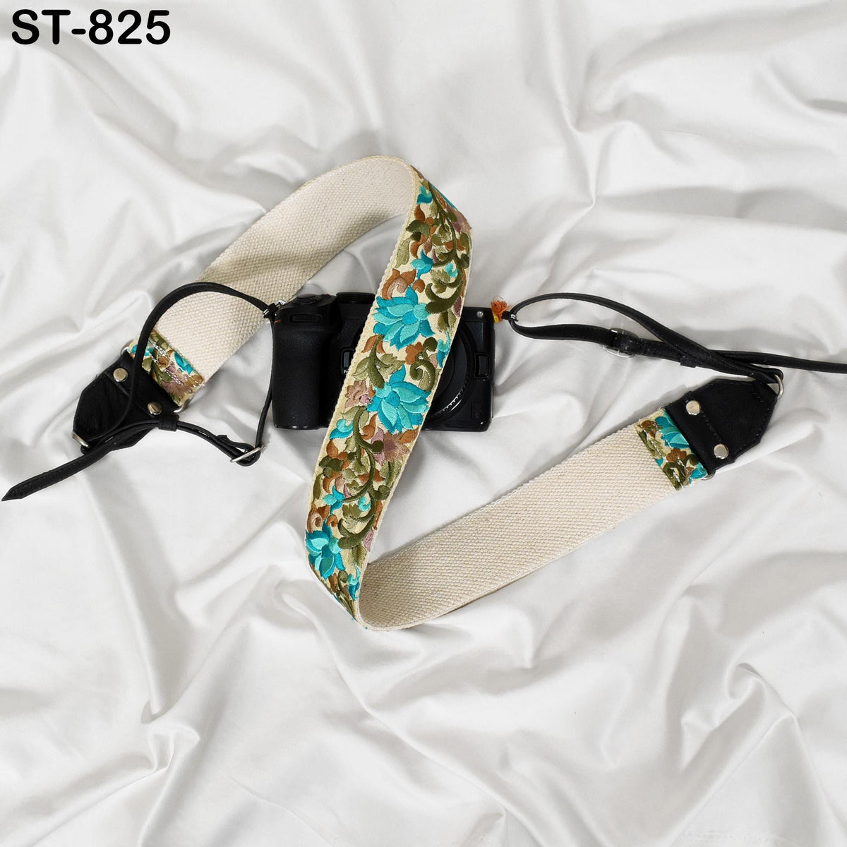 A camera strap with a floral pattern is shown on a white fabric surface.