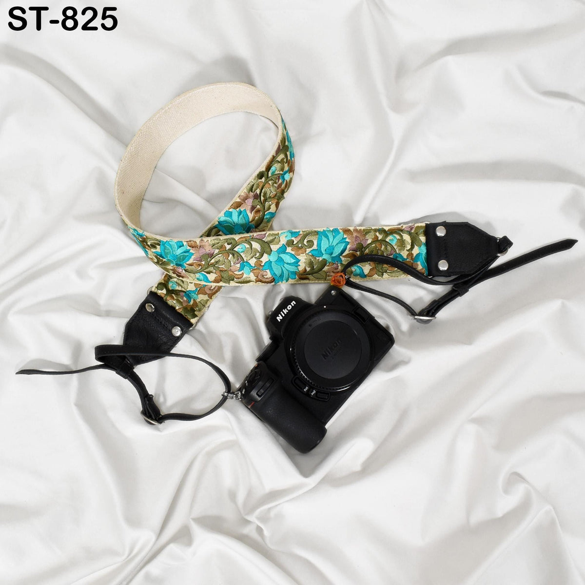 A floral patterned camera strap and a black camera with a lens cap are placed on a white, crumpled surface.