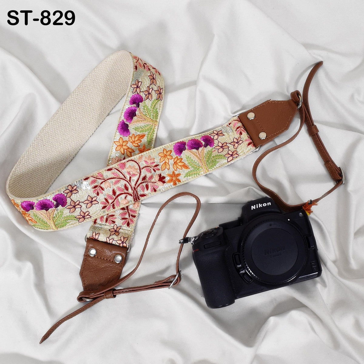 A floral patterned camera strap and a black Nikon camera are placed on a white surface.