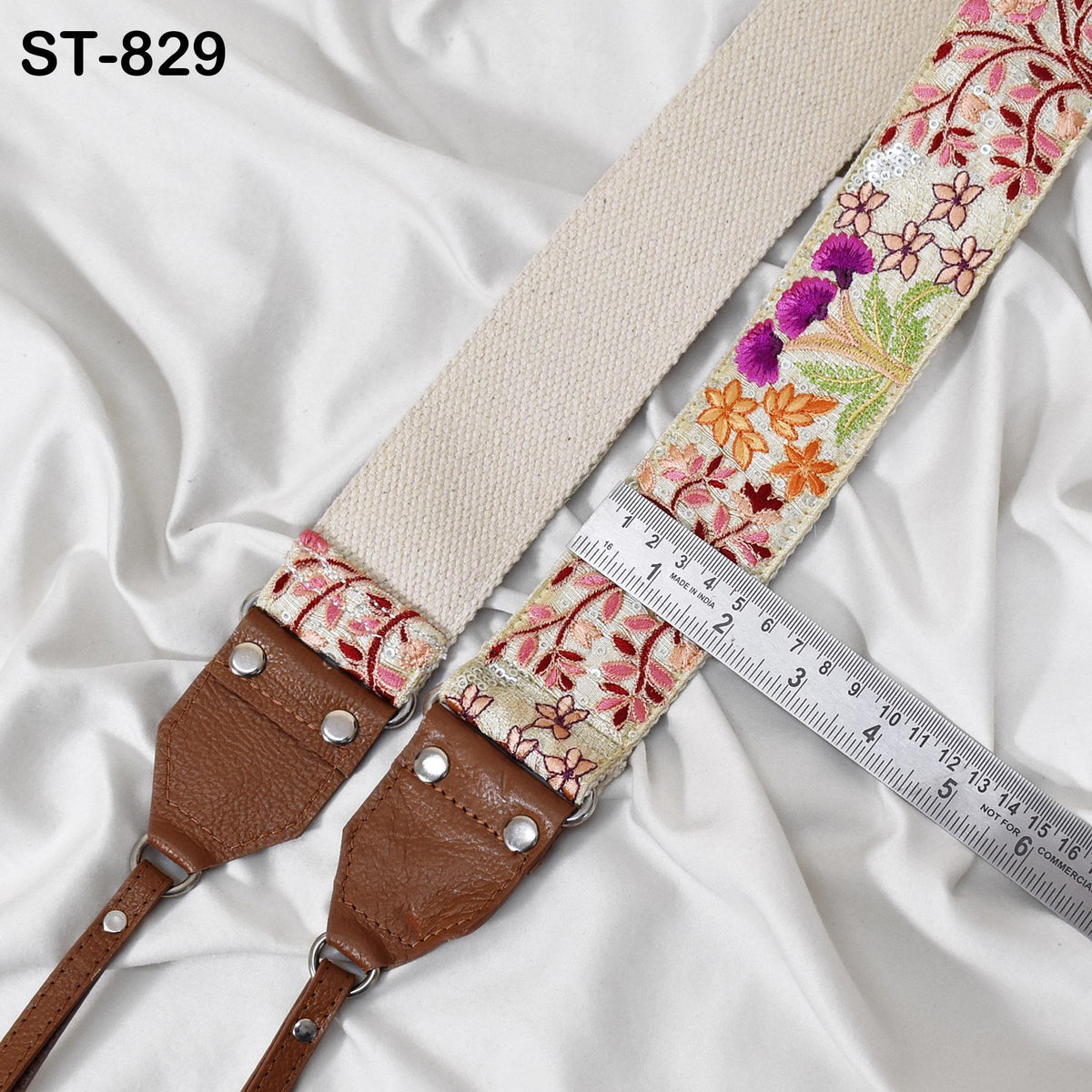 A beige strap with floral embroidery and a leather strap are placed on a white fabric surface, with a ruler for size reference.