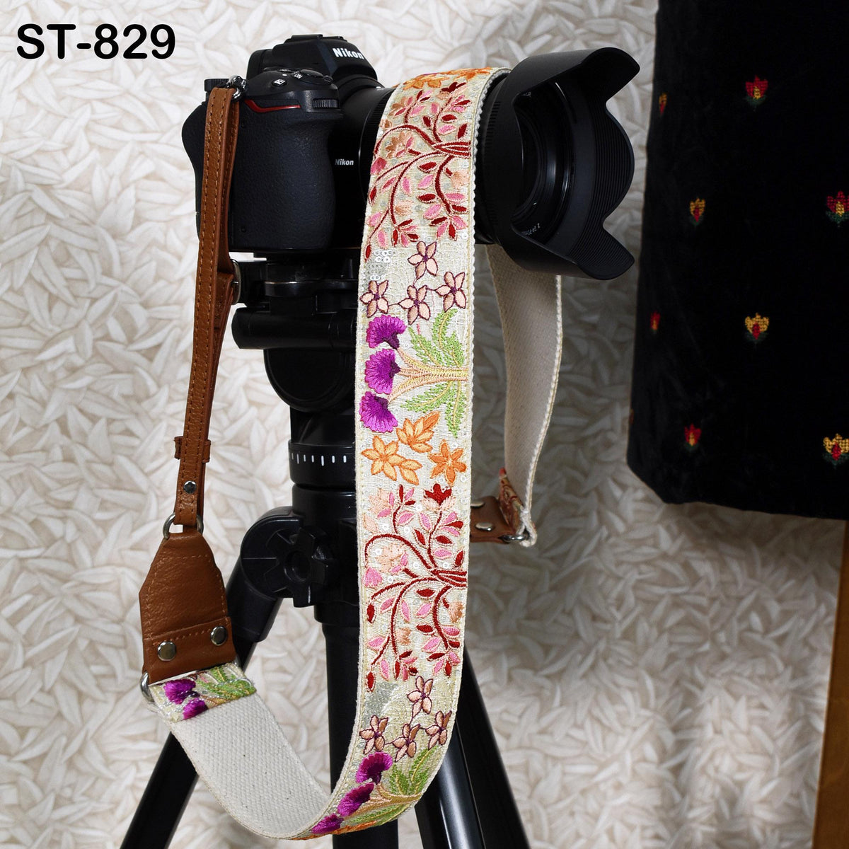 A camera with a floral patterned strap is mounted on a tripod, with a black lens attached to the camera.