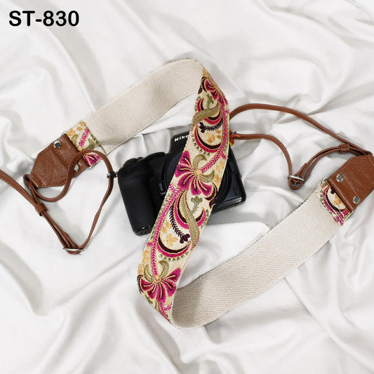 A camera strap with a floral pattern and a black camera resting on a white surface.