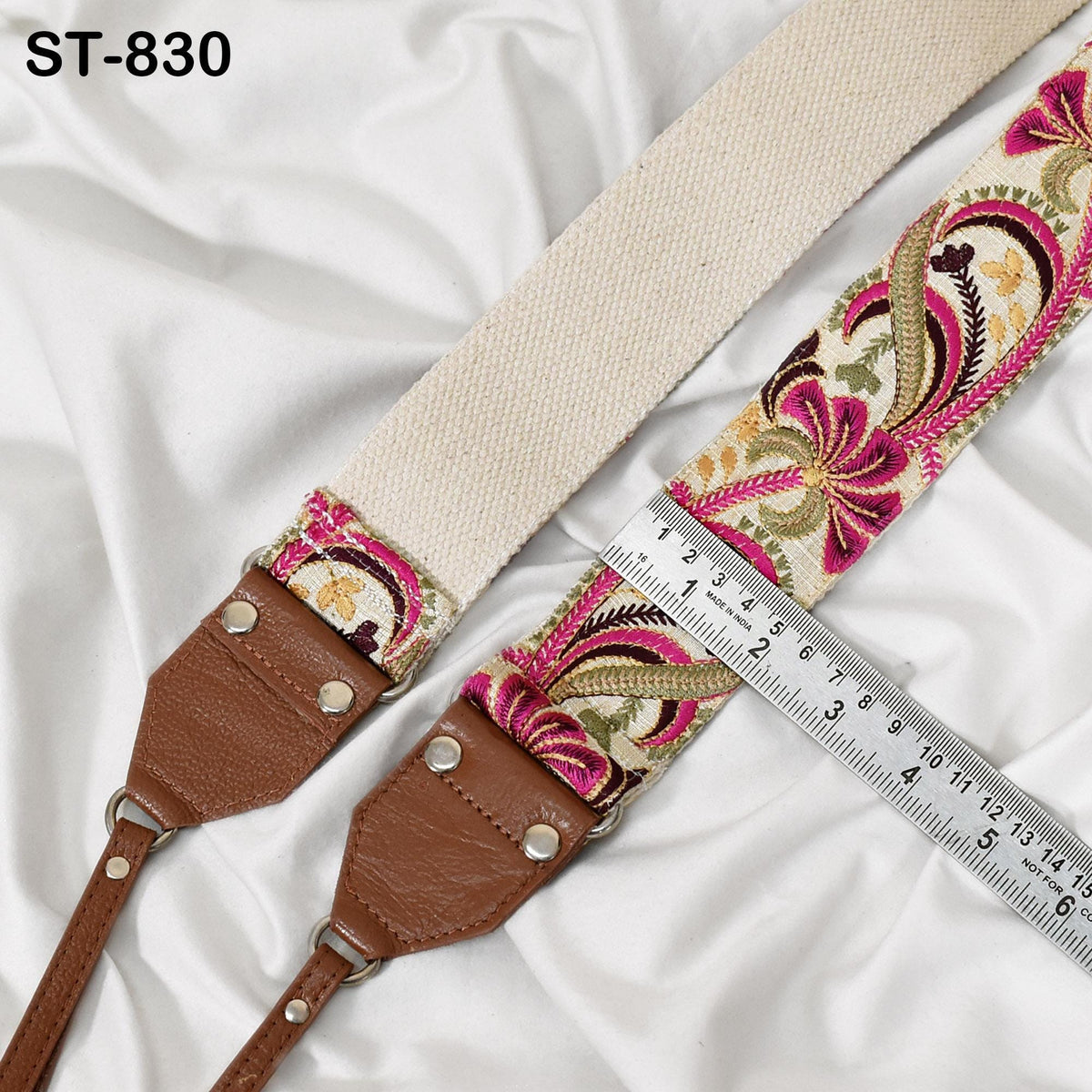 A beige strap with a floral pattern and a brown leather strap are placed on a white fabric surface, with a ruler placed next to them.