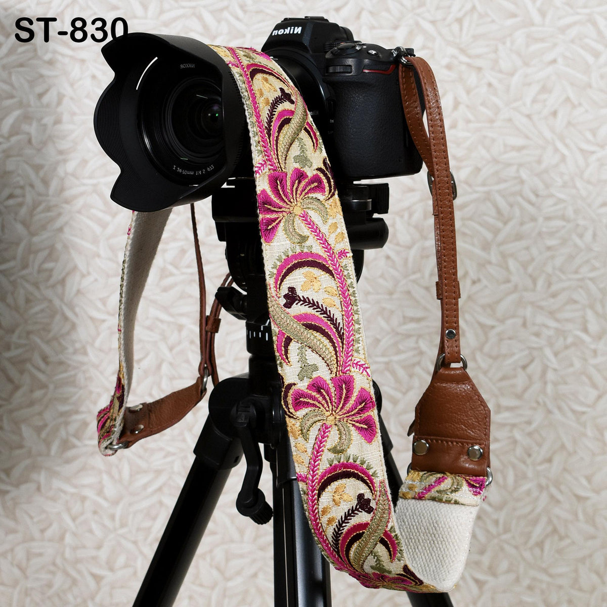 A camera with a floral patterned strap is mounted on a tripod against a patterned background.
