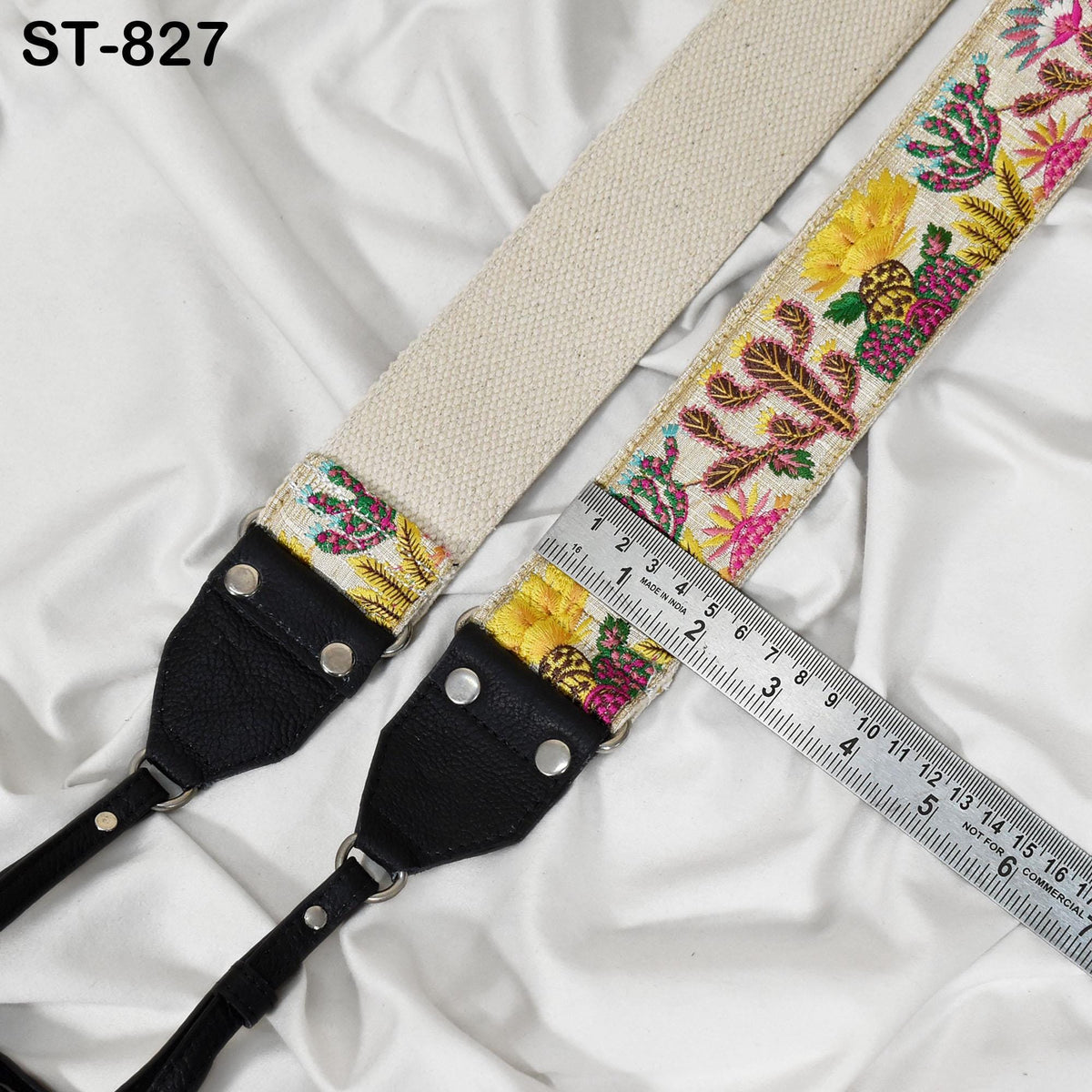 A beige strap with a colorful floral pattern and a black leather strap are placed on a white fabric surface, with a ruler placed next to them.