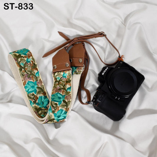 A floral patterned camera strap and a black Nikon camera are placed on a white, crumpled surface.