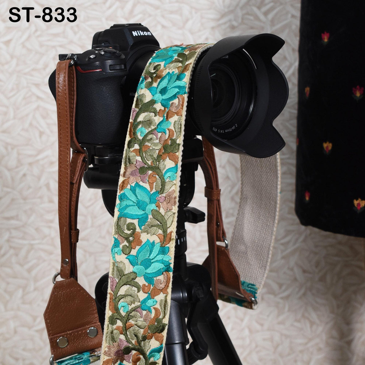 A black camera with a floral patterned strap is mounted on a tripod, with a blurred background.