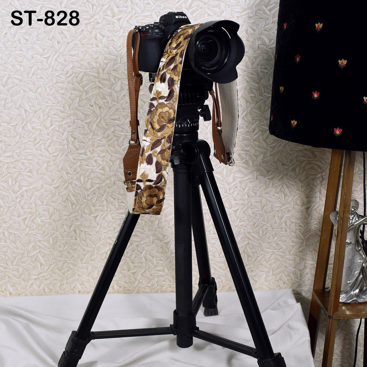 A black tripod with a camera mounted on top, along with a patterned strap, is placed on a white surface.