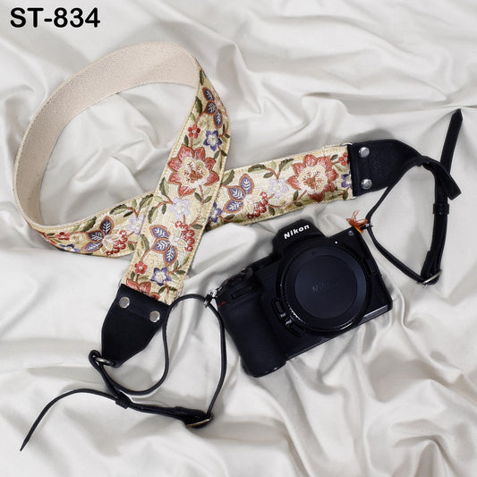 A floral patterned camera strap and a black Nikon camera are placed on a white fabric surface.