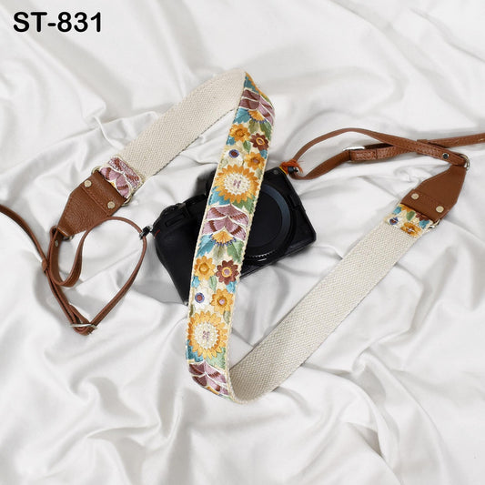 A camera strap with a floral pattern is placed on a white fabric surface.