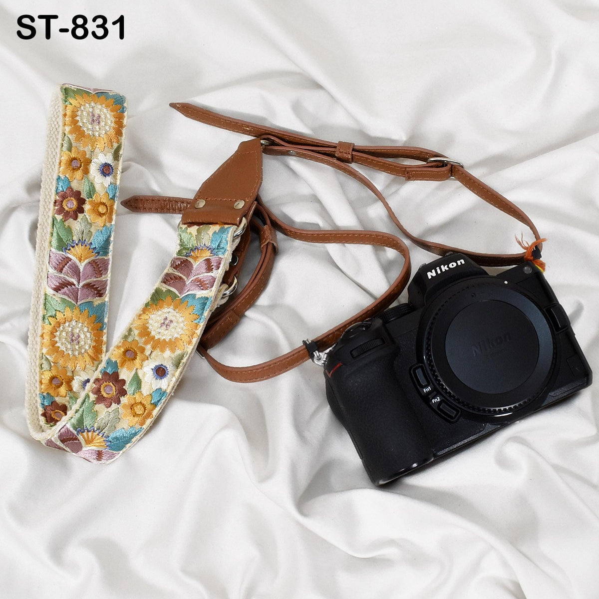 A floral patterned camera strap and a black Nikon camera are placed on a white fabric surface.