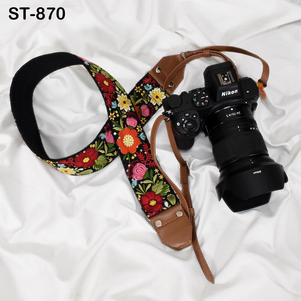 A floral patterned camera strap and a Nikon camera are placed on a white surface.