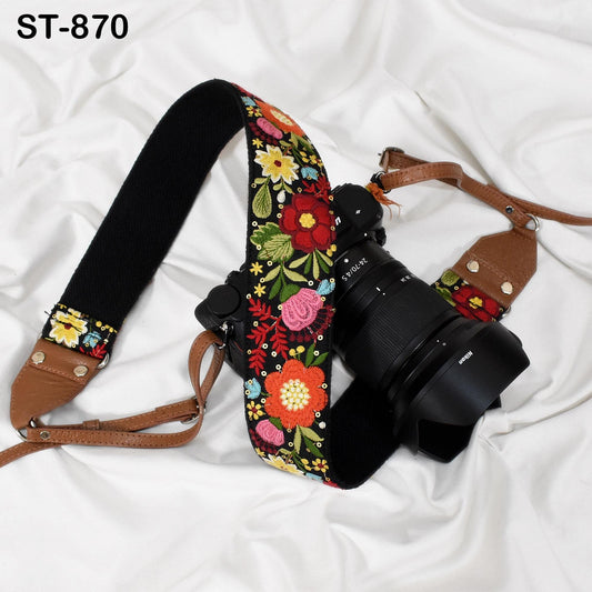 A floral patterned camera strap and a camera lens are placed on a white surface.