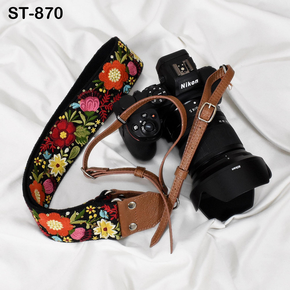 A floral patterned camera strap and a Nikon camera are placed on a white surface.
