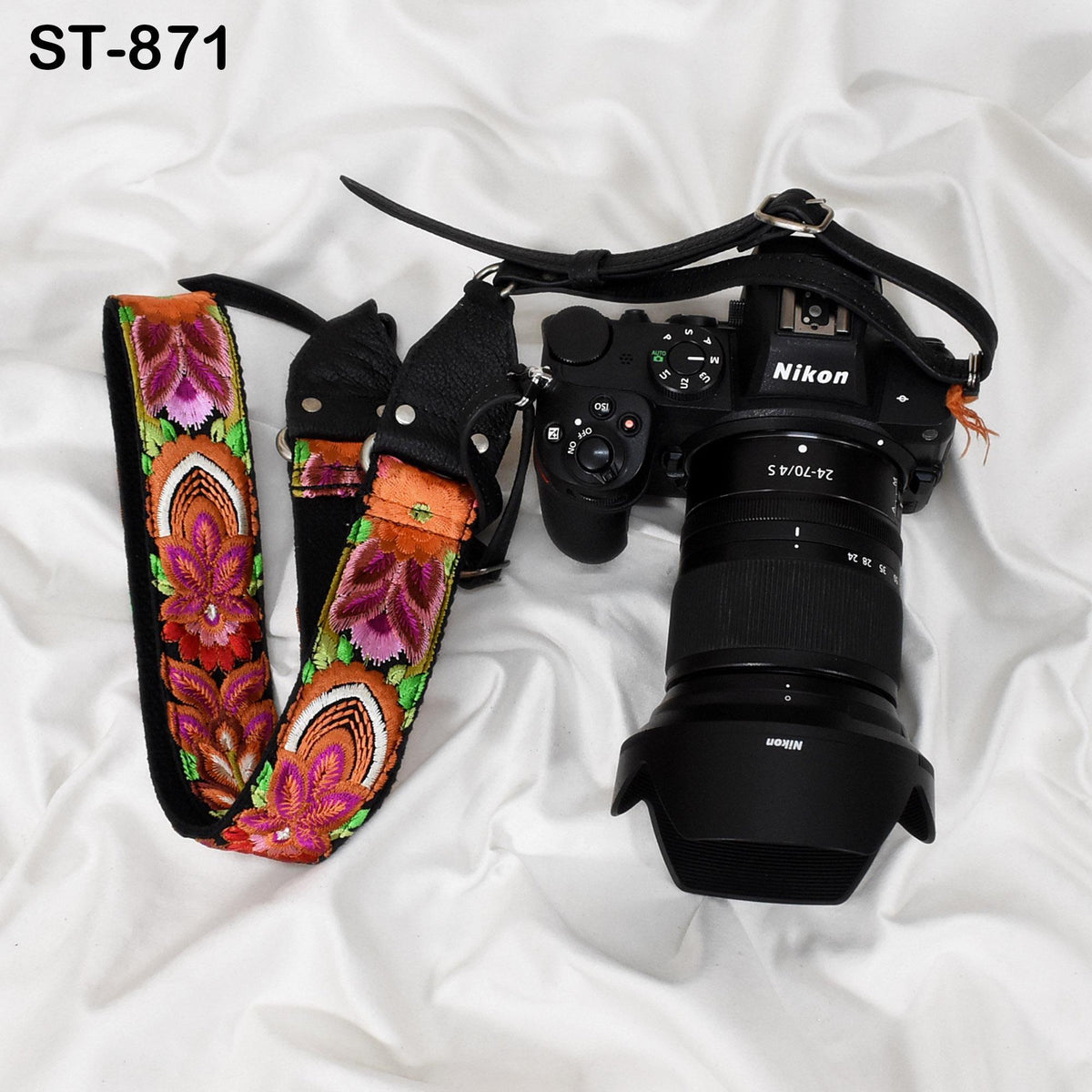 A Nikon camera with a lens attached, along with a colorful patterned strap, is placed on a white surface.