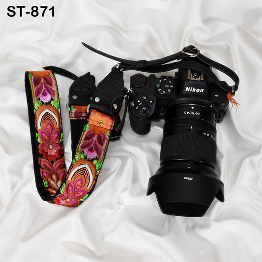 A Nikon camera with a lens attached, along with a colorful patterned strap, is placed on a white surface.
