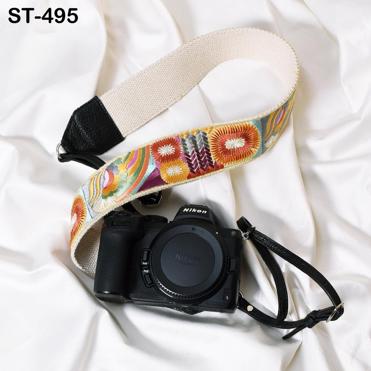A black camera with a colorful strap is placed on a white fabric surface.