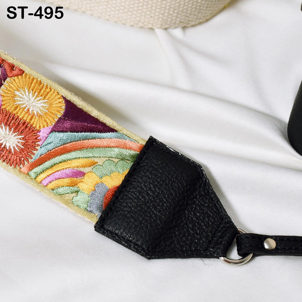A colorful, embroidered strap with a black leather attachment, resting on a white surface.