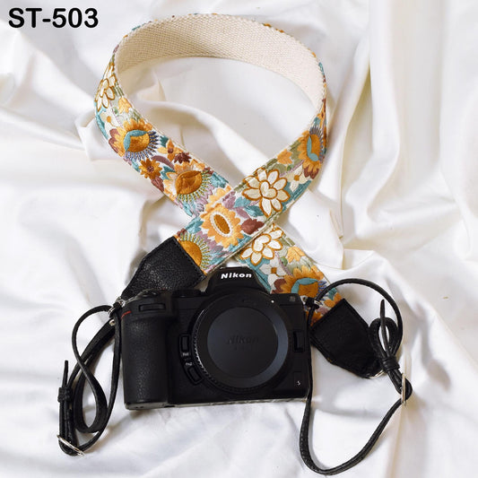 A black camera with a colorful floral strap is placed on a white surface.