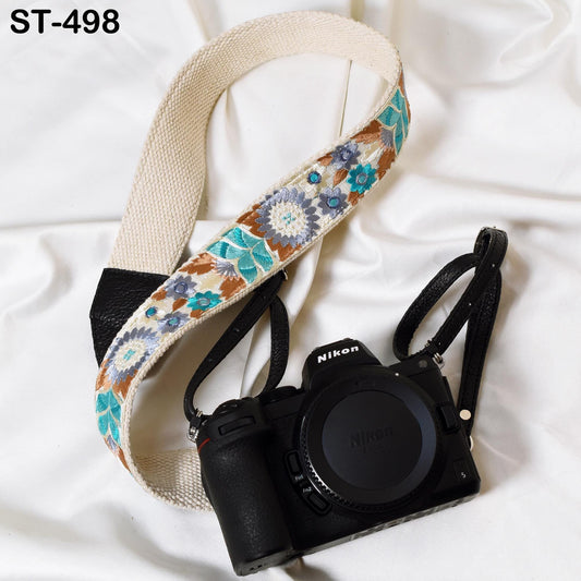 A black Nikon camera with a floral patterned strap is placed on a white surface.