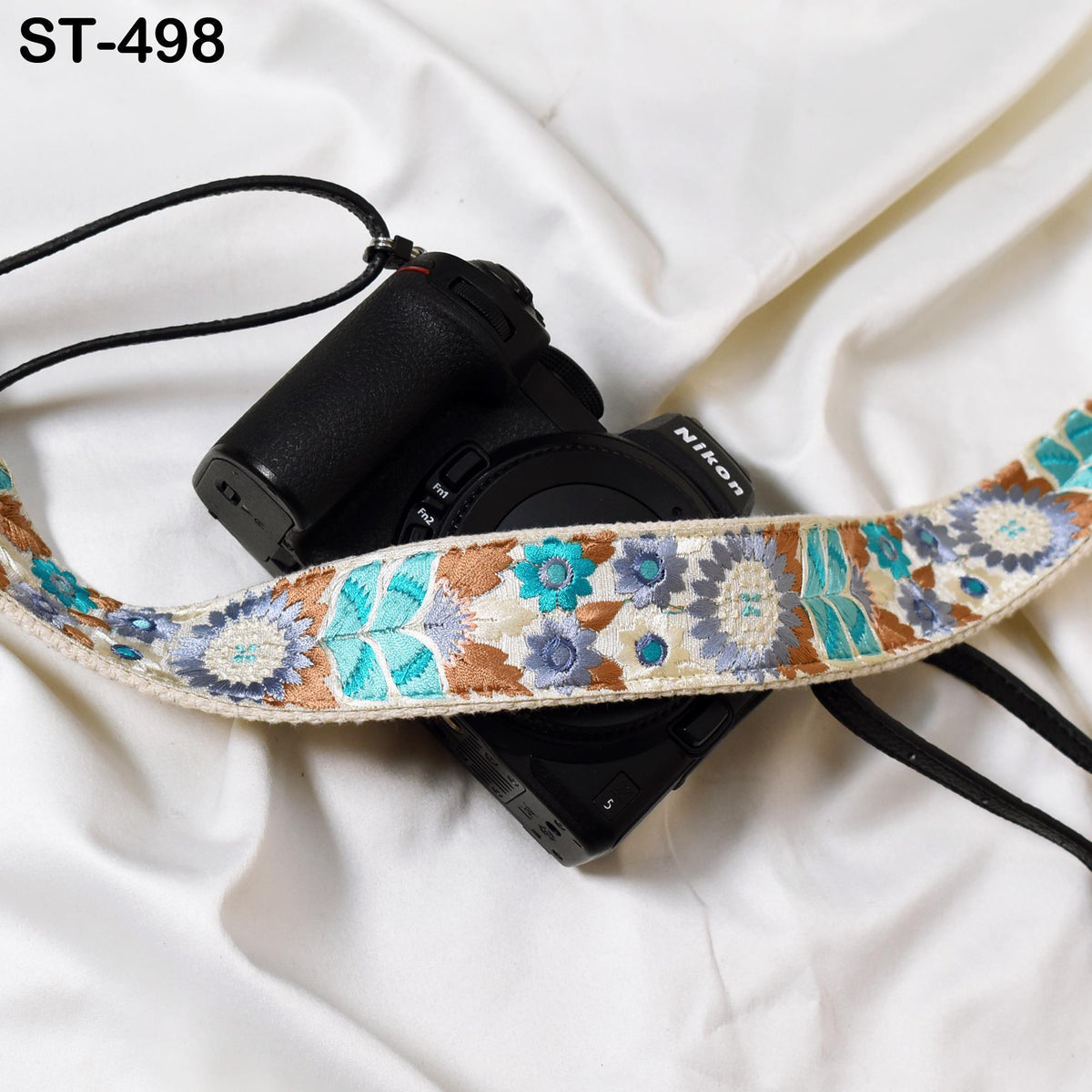 A black camera with a floral patterned strap is placed on a white surface.