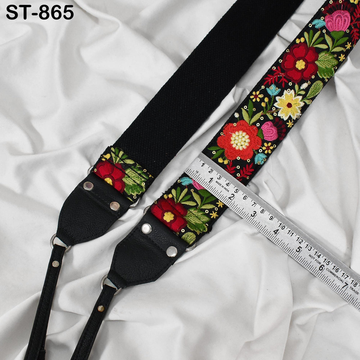 A black camera strap with a floral pattern and a ruler placed on top of it.