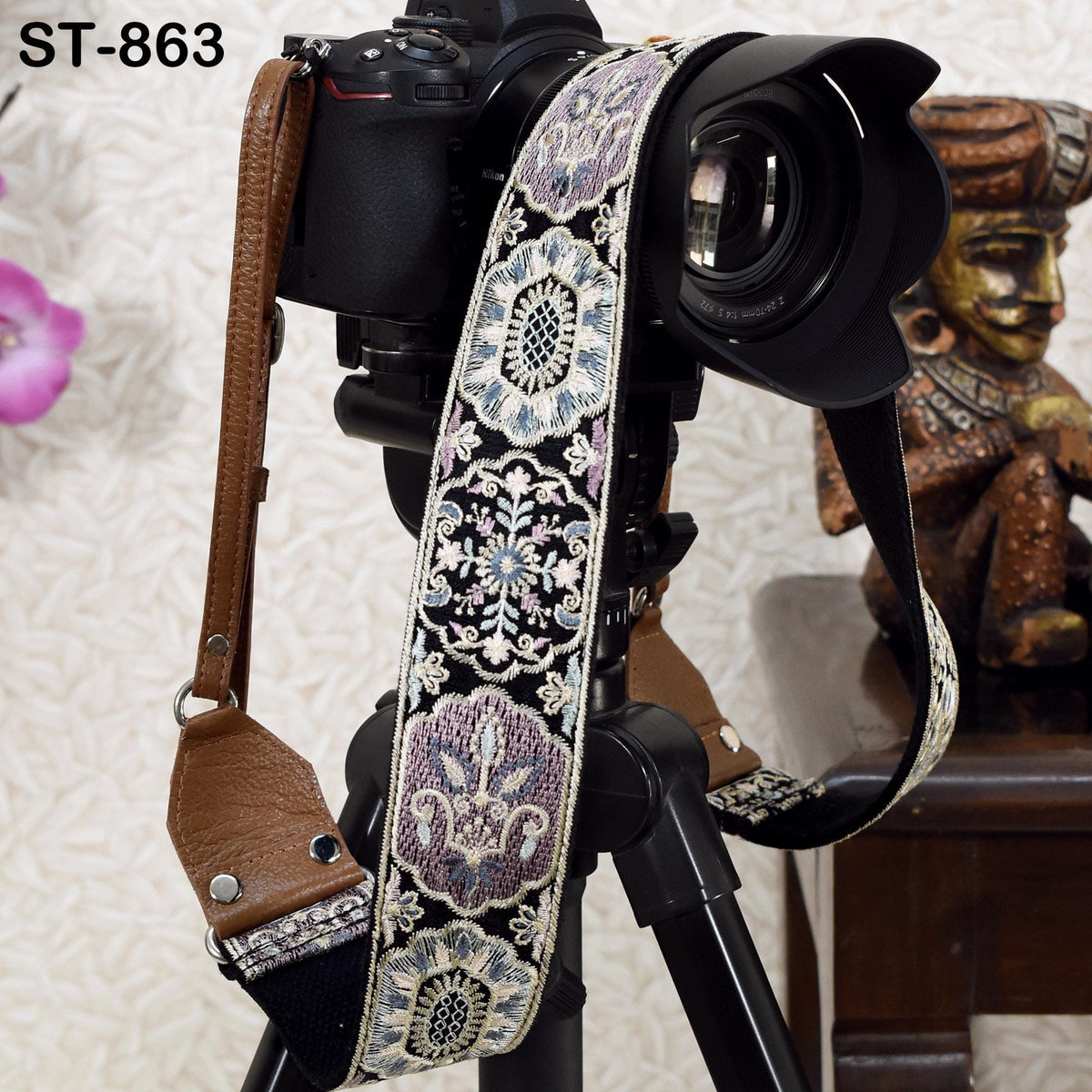 A camera strap with a decorative pattern is attached to a camera, and there is a statue visible in the background.
