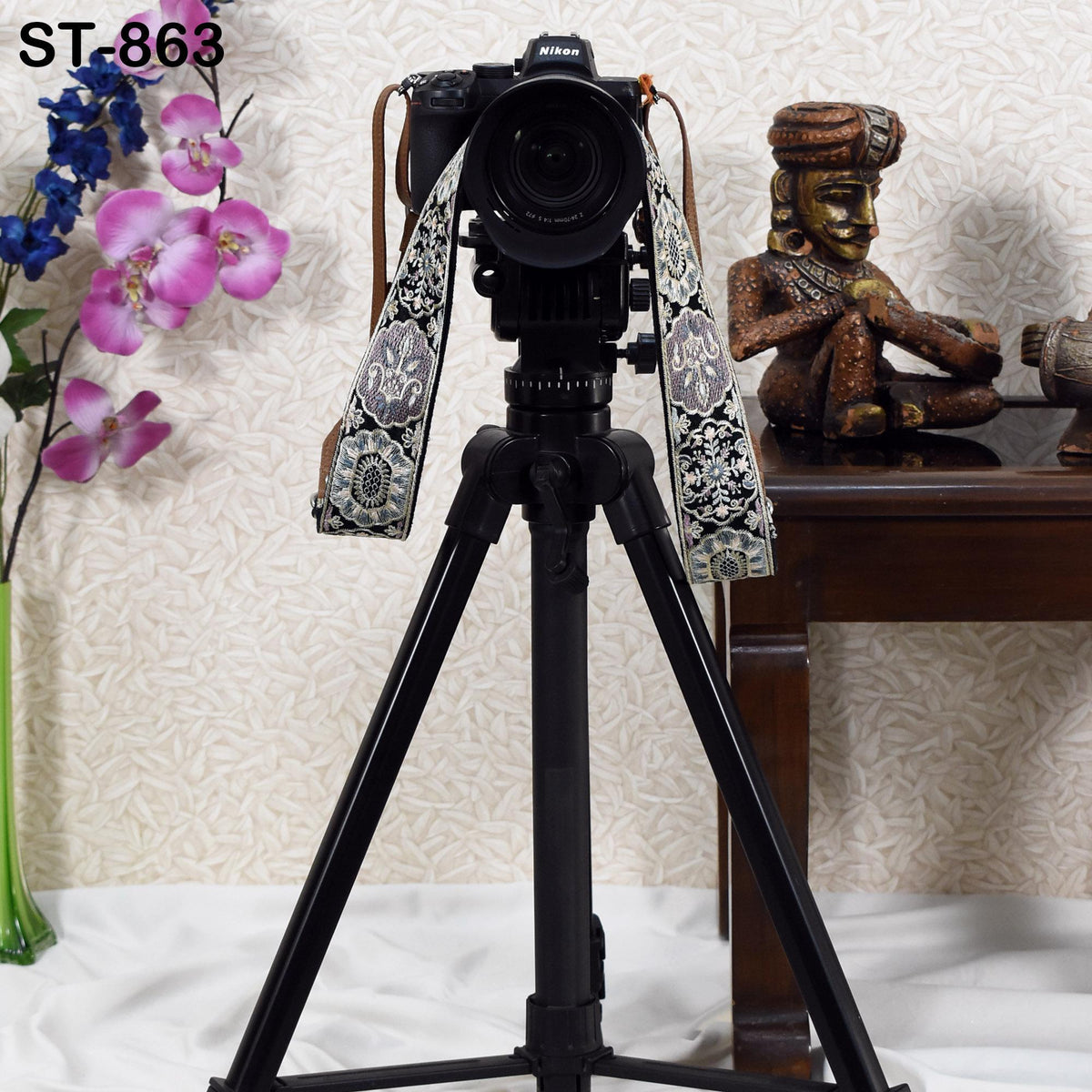a camera with a strap, a tripod, and a decorative statue on a table.