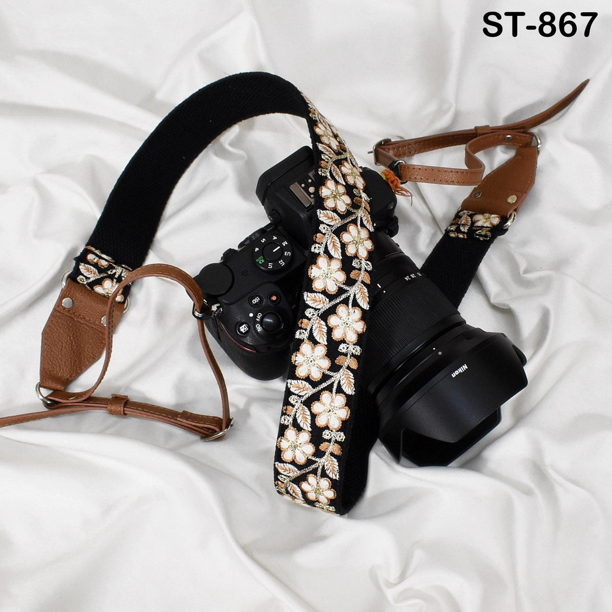 A black camera with a floral patterned strap and a brown leather strap are placed on a white surface.