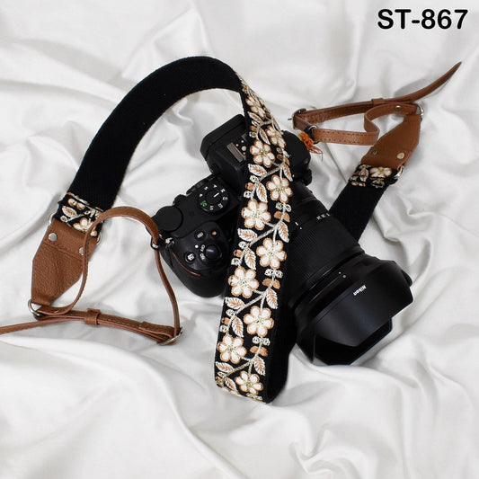 A black camera with a floral patterned strap and a brown leather strap are placed on a white surface.