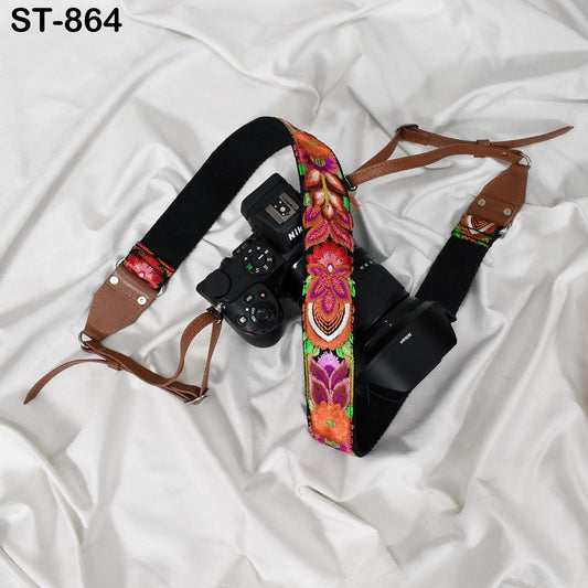 A black camera strap with a colorful floral pattern is attached to a camera, resting on a white fabric surface.