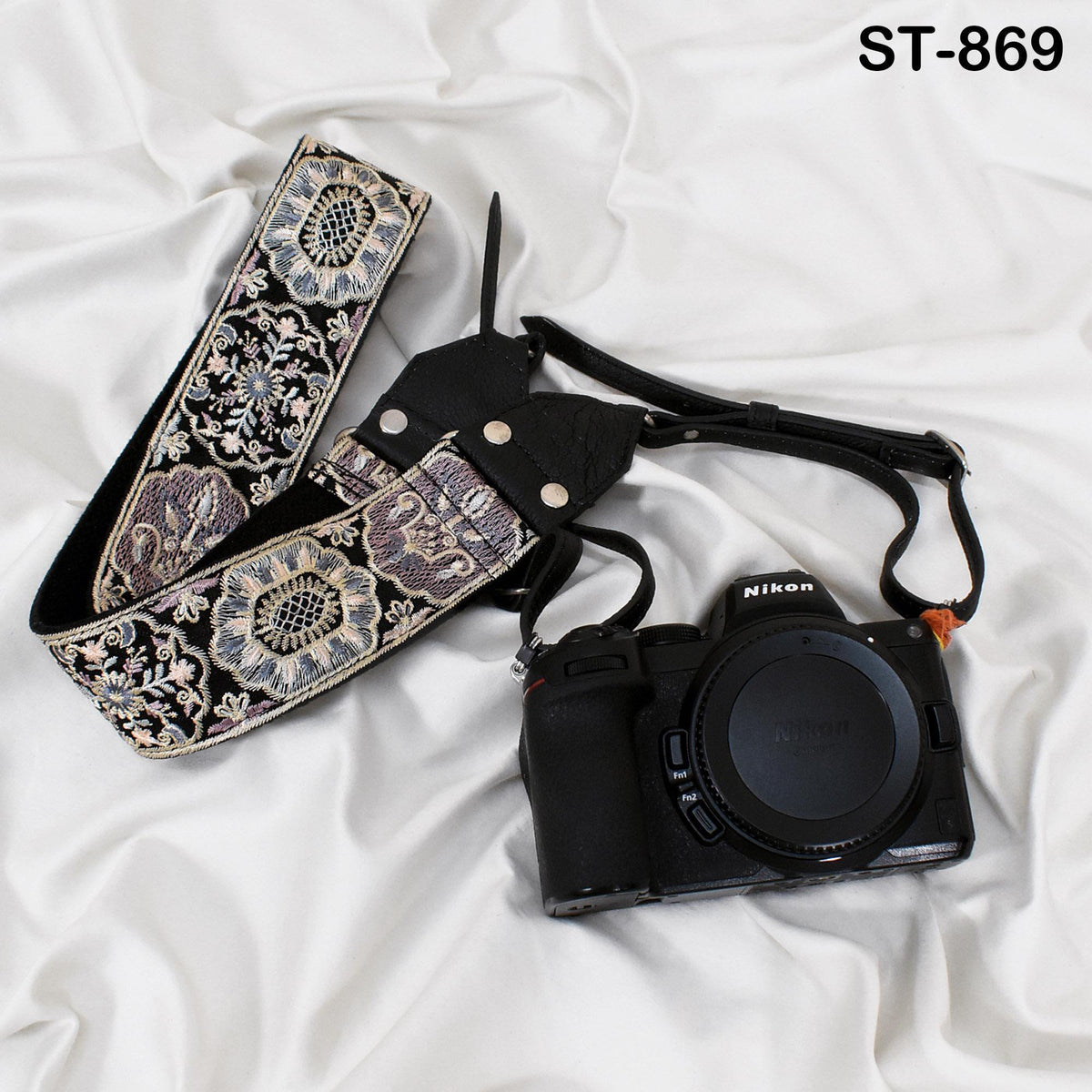 A black camera with a floral patterned strap is placed on a white surface.
