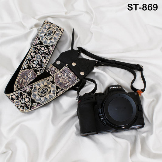 A black camera with a floral patterned strap is placed on a white surface.
