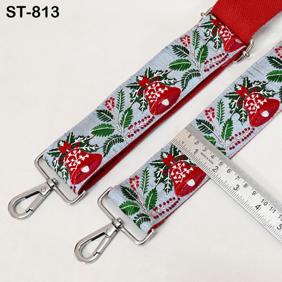 A decorative Christmas-themed fabric strap with a red buckle, featuring a floral pattern and bell motifs, is shown alongside a ruler for size comparison.