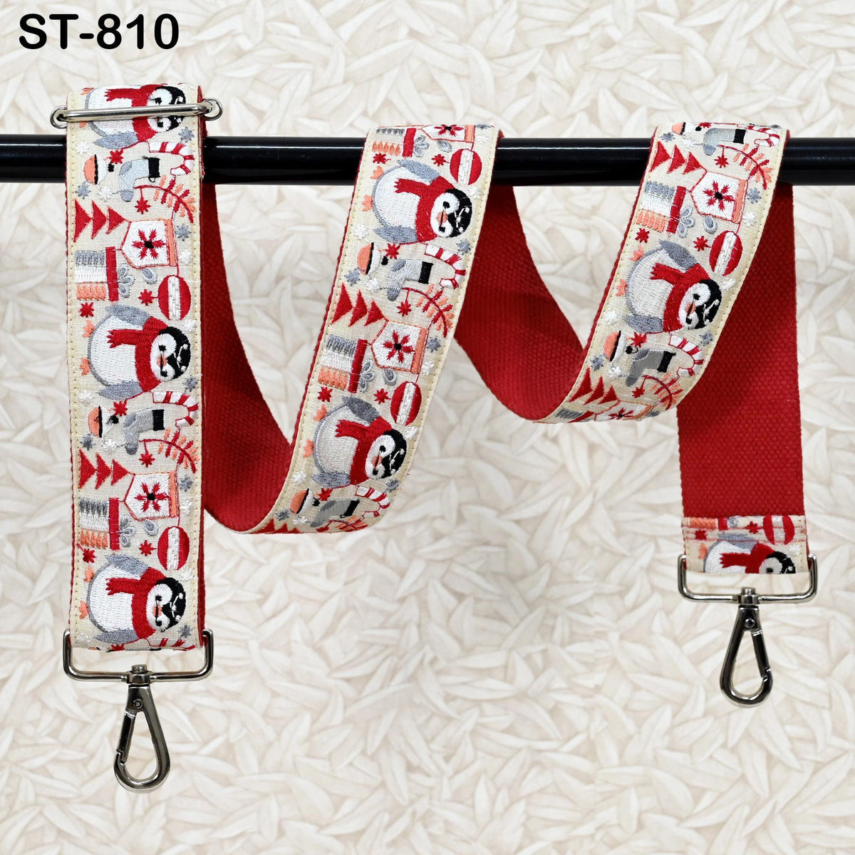 A red and white patterned strap with a snowman design and Christmas-themed elements, hanging on a black pole.