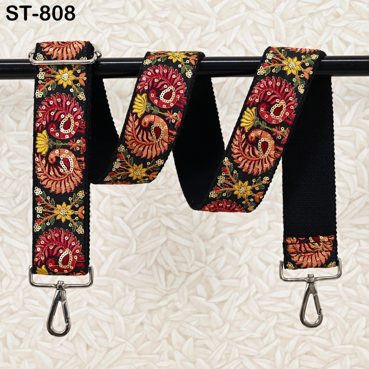 A colorful, patterned strap with floral designs is hanging on a black metal hook.