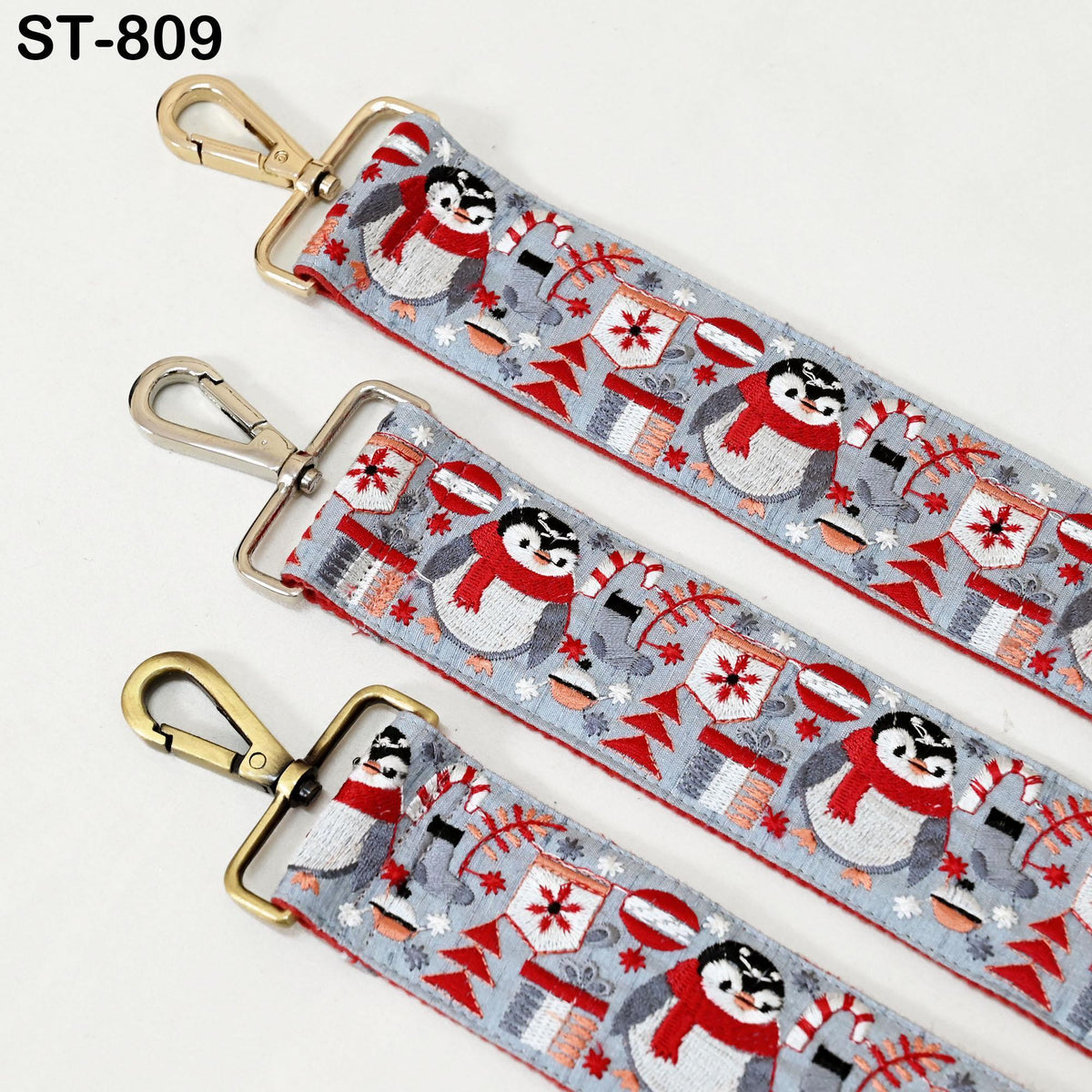 three straps with a festive pattern of penguins and snowflakes. The straps have a metallic hook and a decorative design featuring red and white elements.