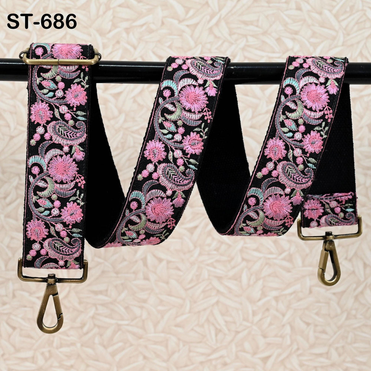 A floral patterned strap with a black background and pink flowers, hanging on a black rod.