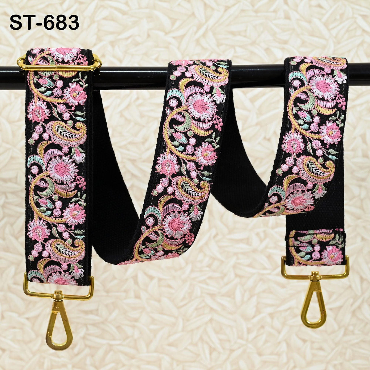 A floral patterned black strap with gold hardware, hanging on a black rod.