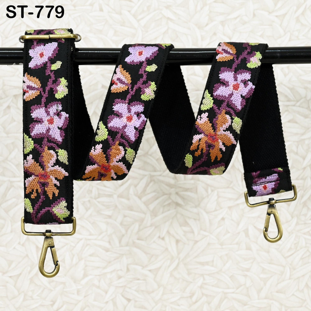 A colorful floral-patterned strap with a black metal buckle, hanging on a black metal bar.