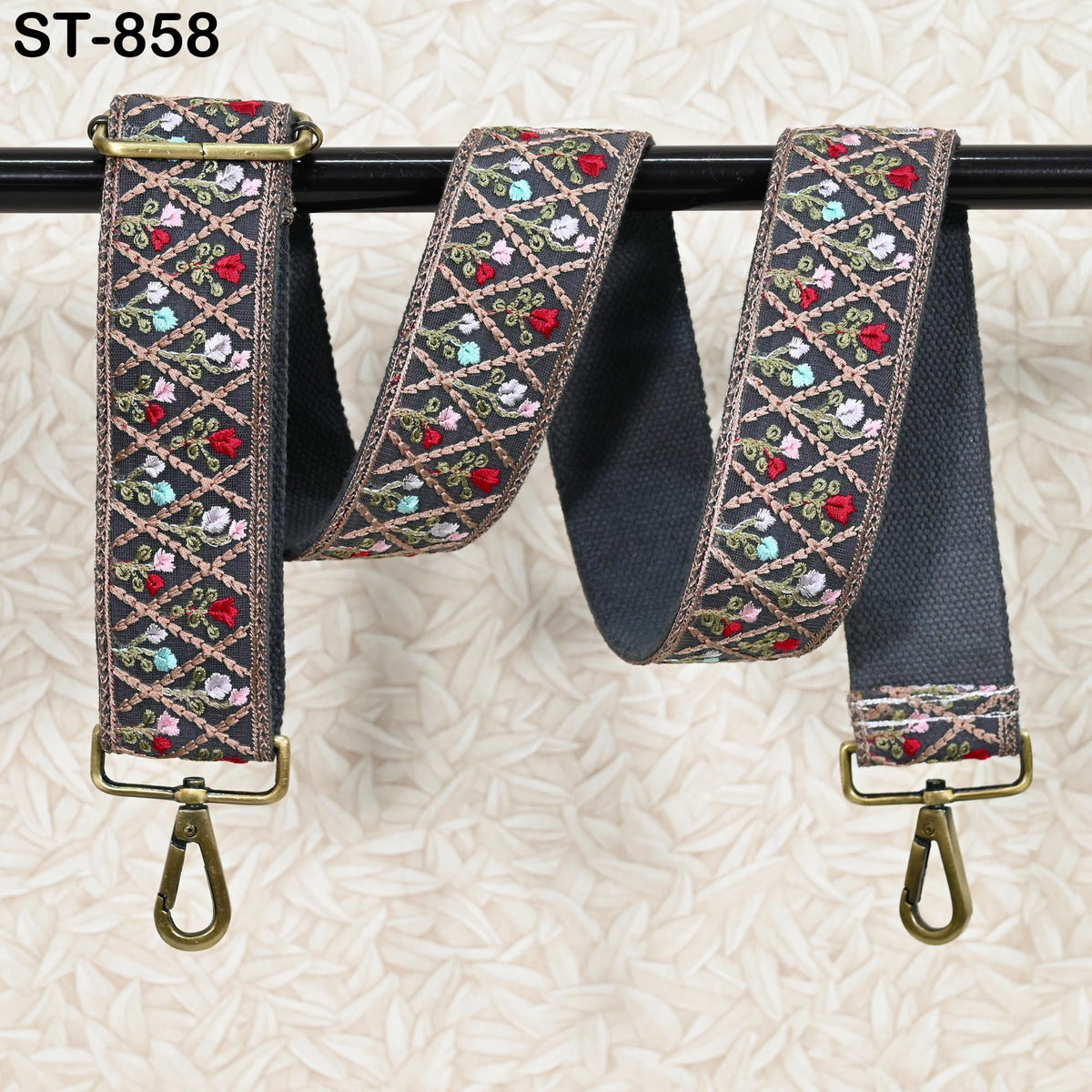 A decorative floral patterned strap with a metal clasp and hook attached to a black metal bar.